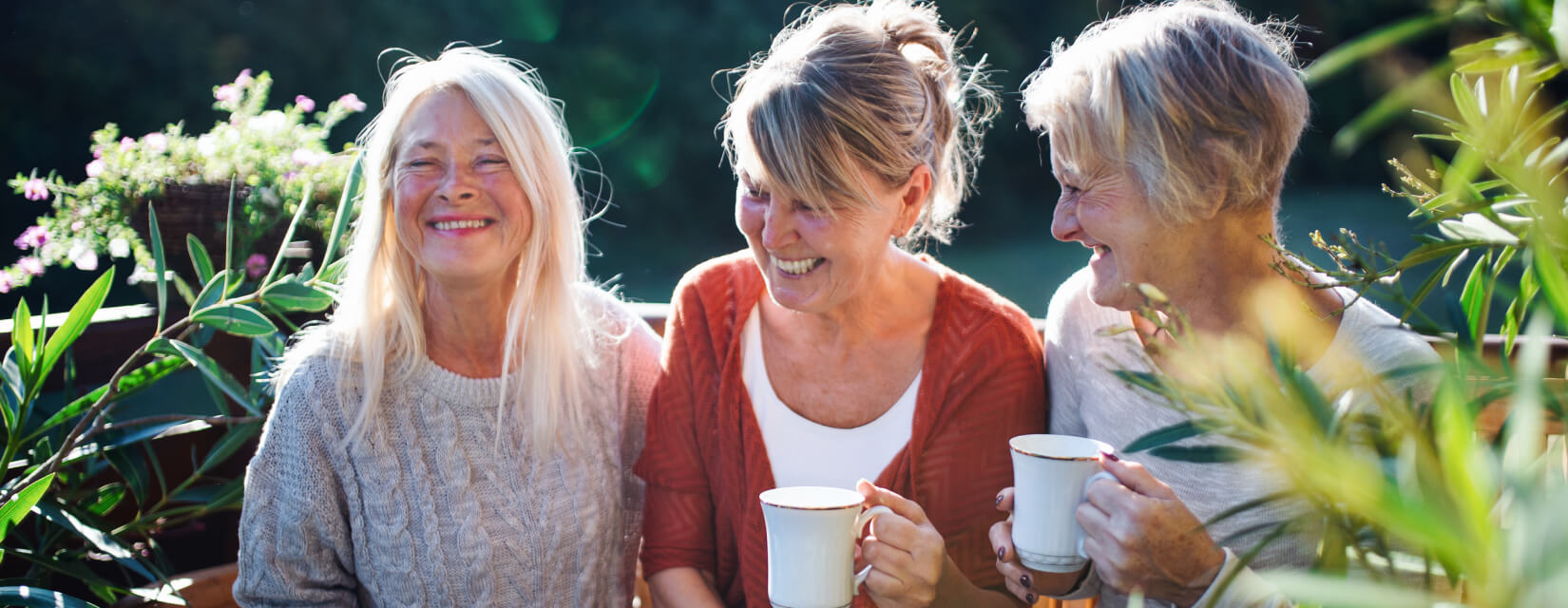 Senior women friends with coffee sitting outdoors on terrace, resting