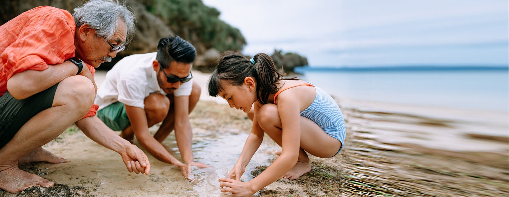 Grandfather, father and girl playing in the sand at the beach