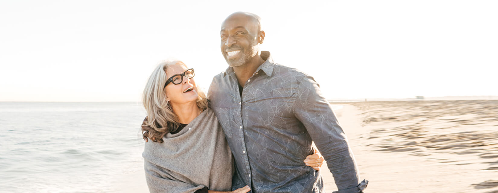 Happy older couple walking arm in arm along a beach on a sunny day