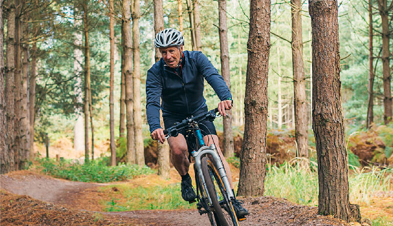A man in his later years mountain biking through the woods