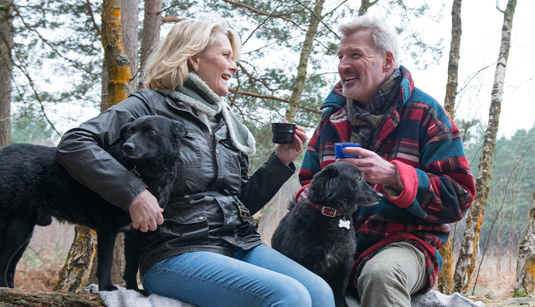 happy couple having a hot drink in the woods with two dogs