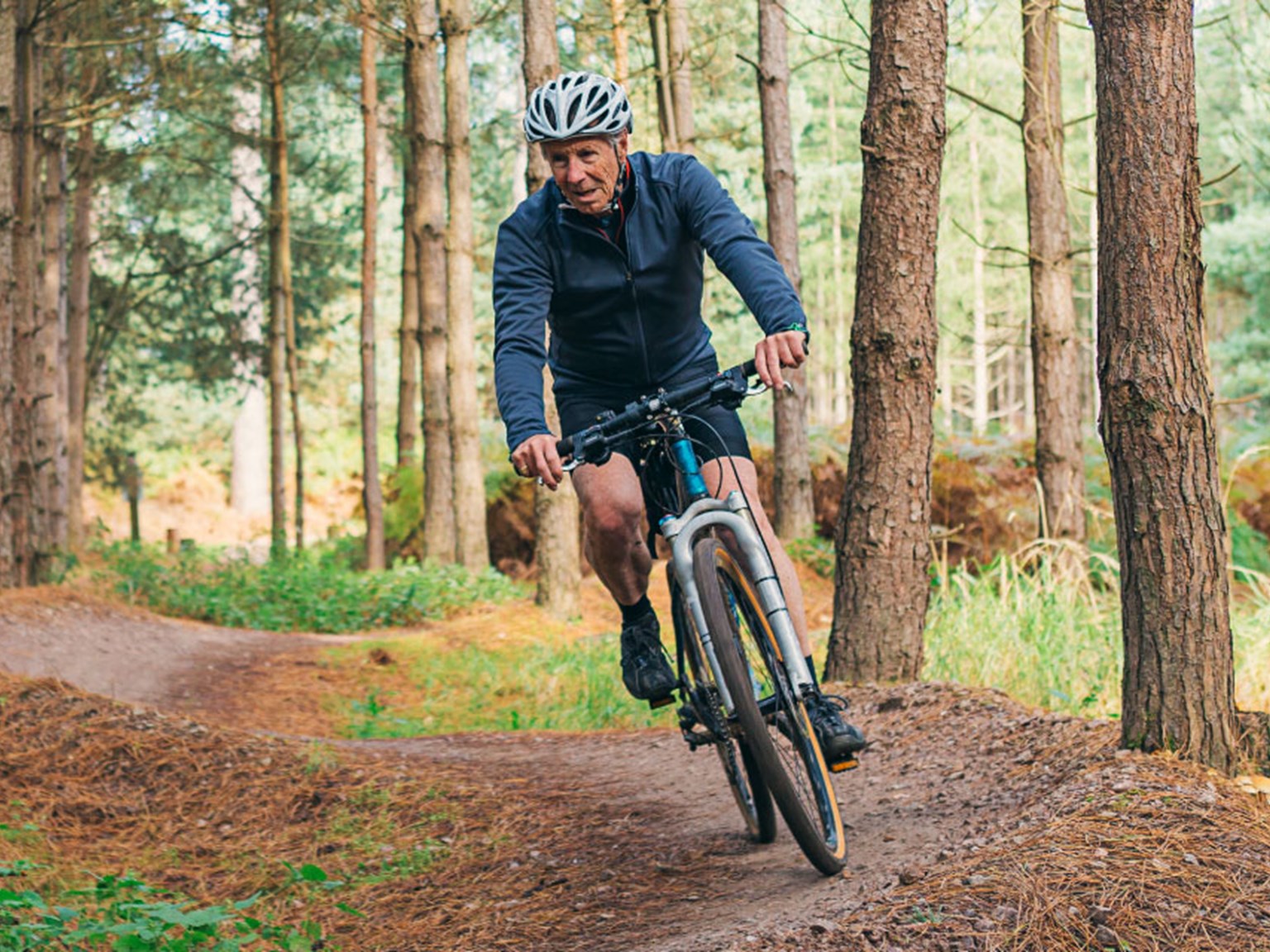 A man in his later years mountain biking through the woods