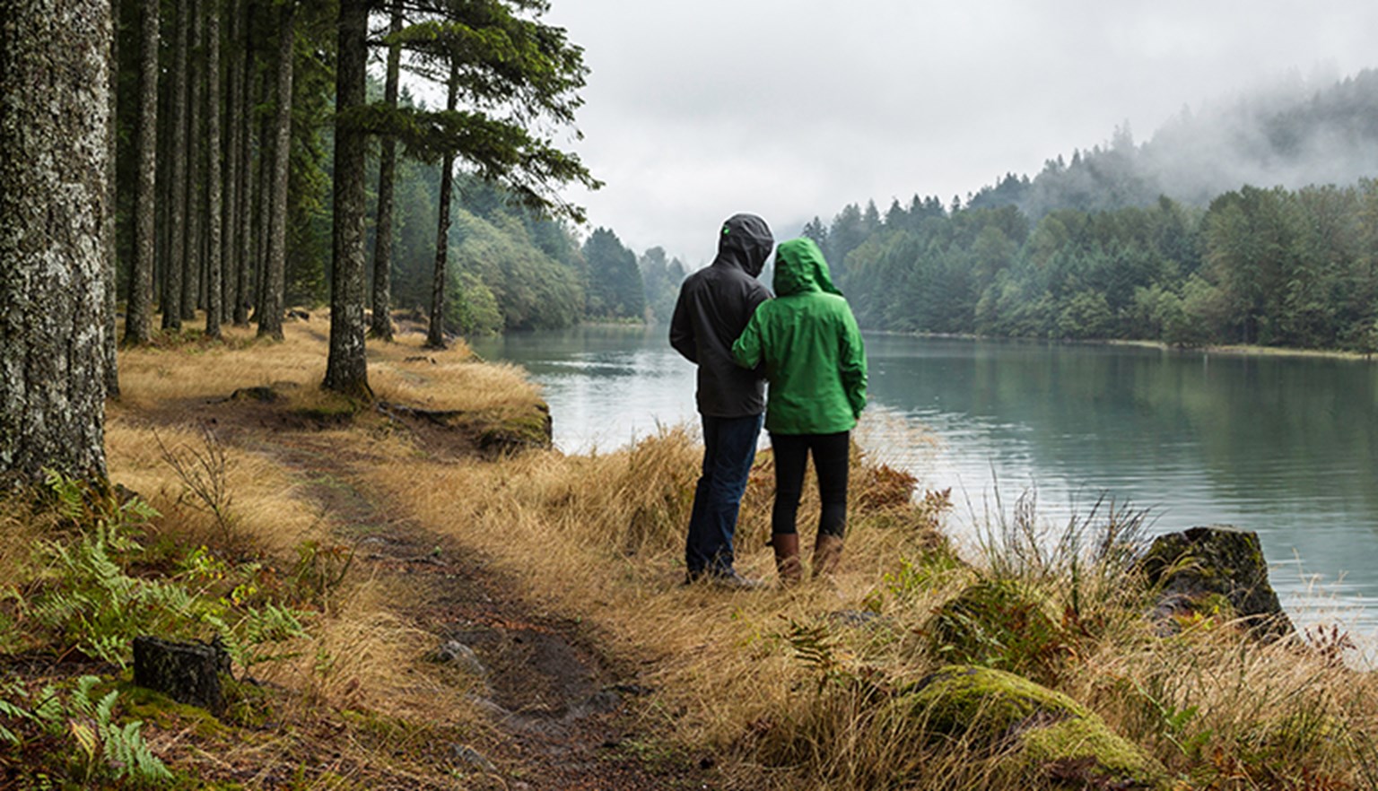 couple stood facing a lake on a rainy day in the woods