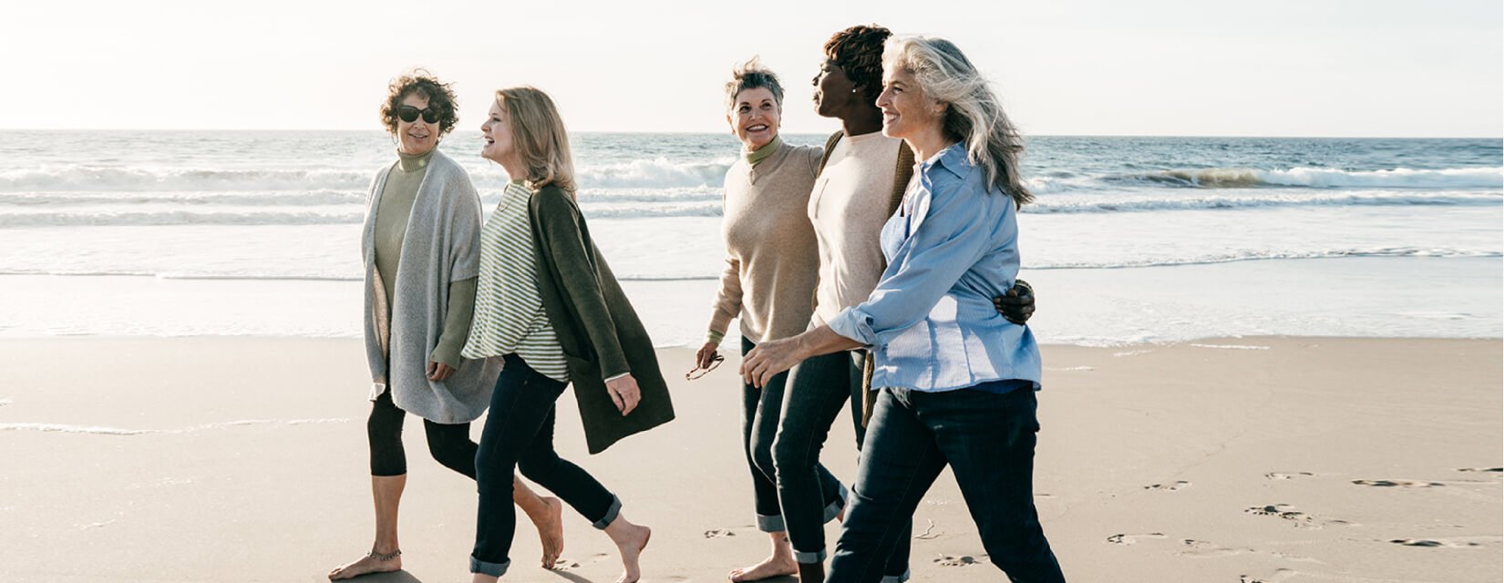 A group of five women in their 50s and 60s walking together on the beach