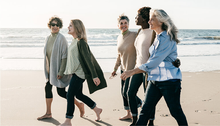 a group of five women in their 50s and 60s walking together on the beach
