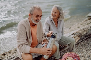 Senior couple sitting on the beach with a flask