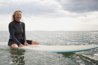 Happy senior woman sat on surfboard on a cloudy day