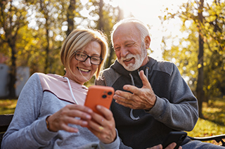 Older couple sat on a park bench enjoying something the woman is showing on her phone