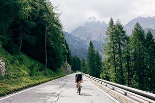 Professional road cyclist on fast and light carbon bicycle descends mountain road in Alps Dolomites. Fit and athletic man on recreational ride trip or training camp, enjoy time outdoors on bike