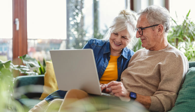 Happy older couple relaxing on a safa with a laptop