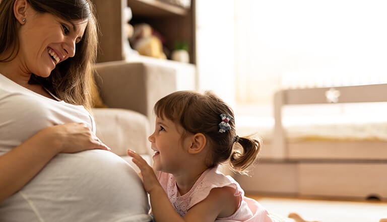 young girl touching pregnant ladies tummy and smiling