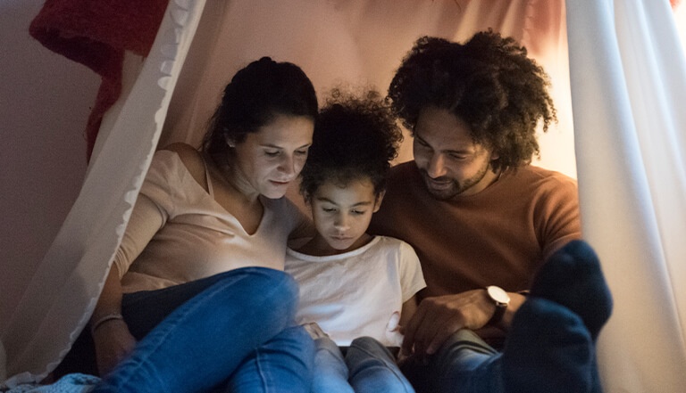 man woman and child sat under a tent reading a book