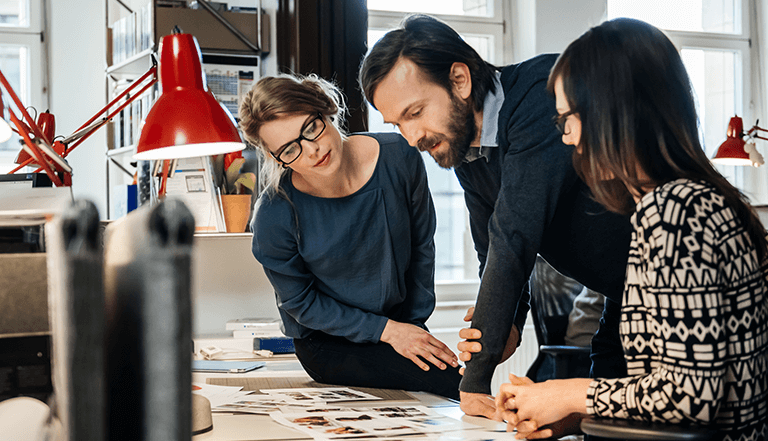 Three people at a desk looking at photos
