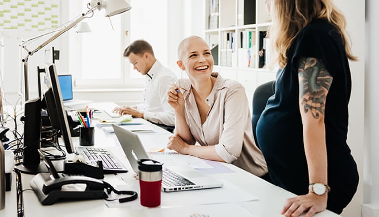 Man and two women in office, pregnant women having a talk with other woman at office desks 