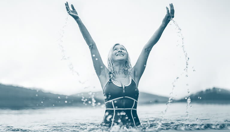 smiling woman in swimming costume in sea with arms in the air