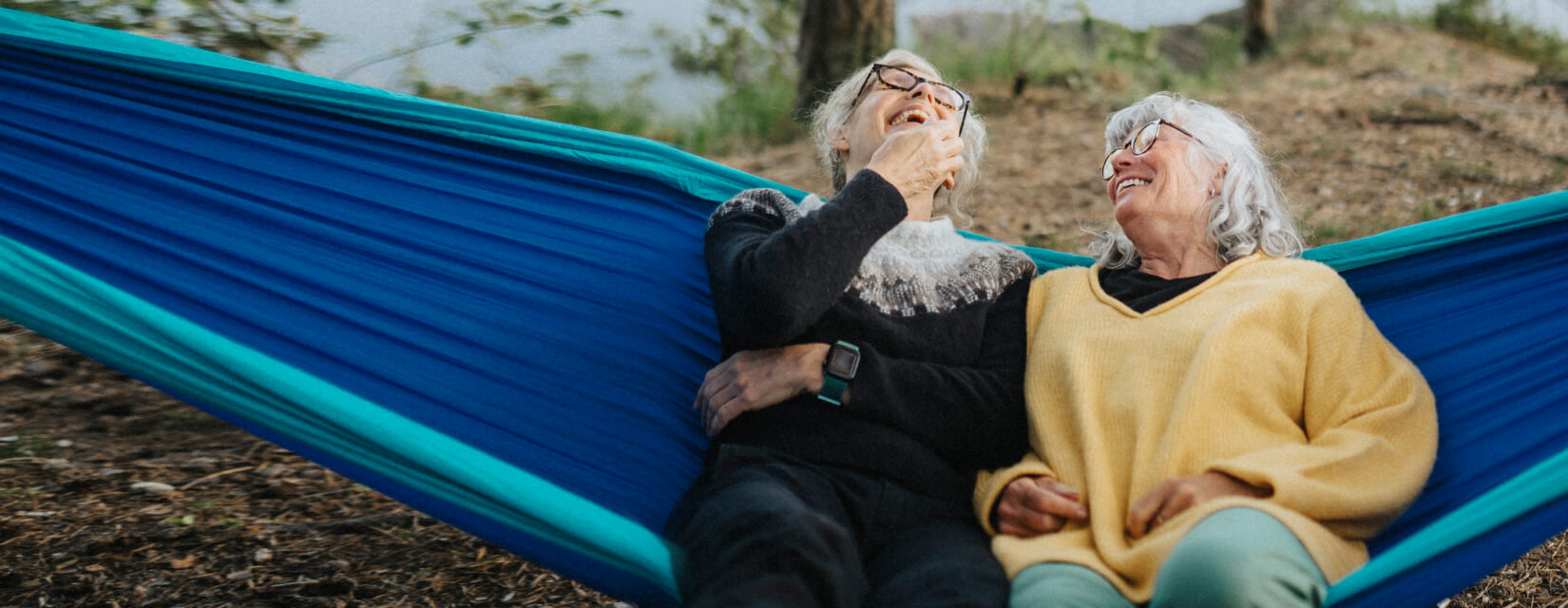 Two friends laughing whilst sitting in a hammock