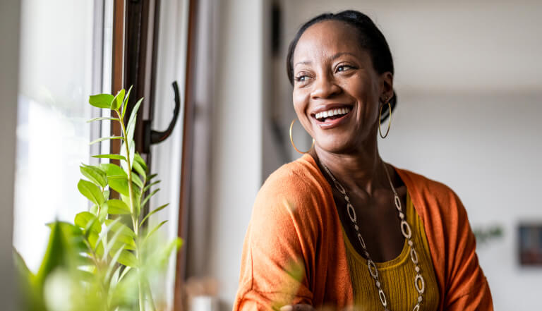 A woman near retirement age smiling and laughing as she looks out of the window. 