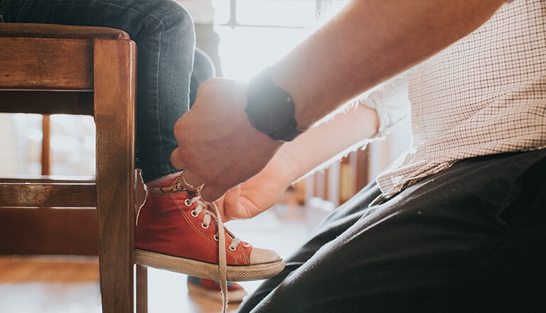 Man tying shoe laces of child